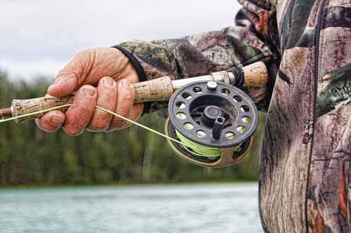 A fisherman holds a rod by a lake